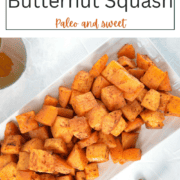 Roasted cubes of golden-orange butternut squash glazed with maple syrup and cinnamon on a white rectangular plate with cinnamon sticks.
