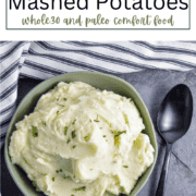 A close-up of a white bowl filled with fluffy, smooth mashed potatoes, topped with fresh green chives and a sprinkle of black pepper.
