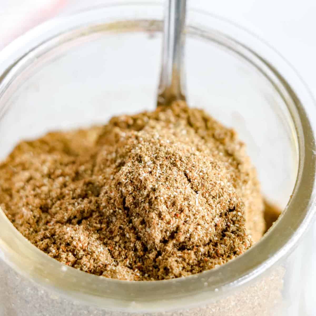 Sage Pork Rub Spices mixed together in a clear dish with a spoon being pulled out. www.atwistedplate.com/sage-pork-rub/