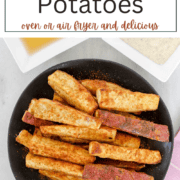 A plate of crispy, thick-cut roasted sweet potato wedges seasoned with Old Bay, served with small bowls of ranch dressing and apple cider vinegar.