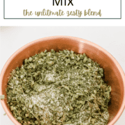 A small copper bowl filled with a blend of dried green herbs and white spices, including chives, parsley, and garlic powder, against a clean white background.
