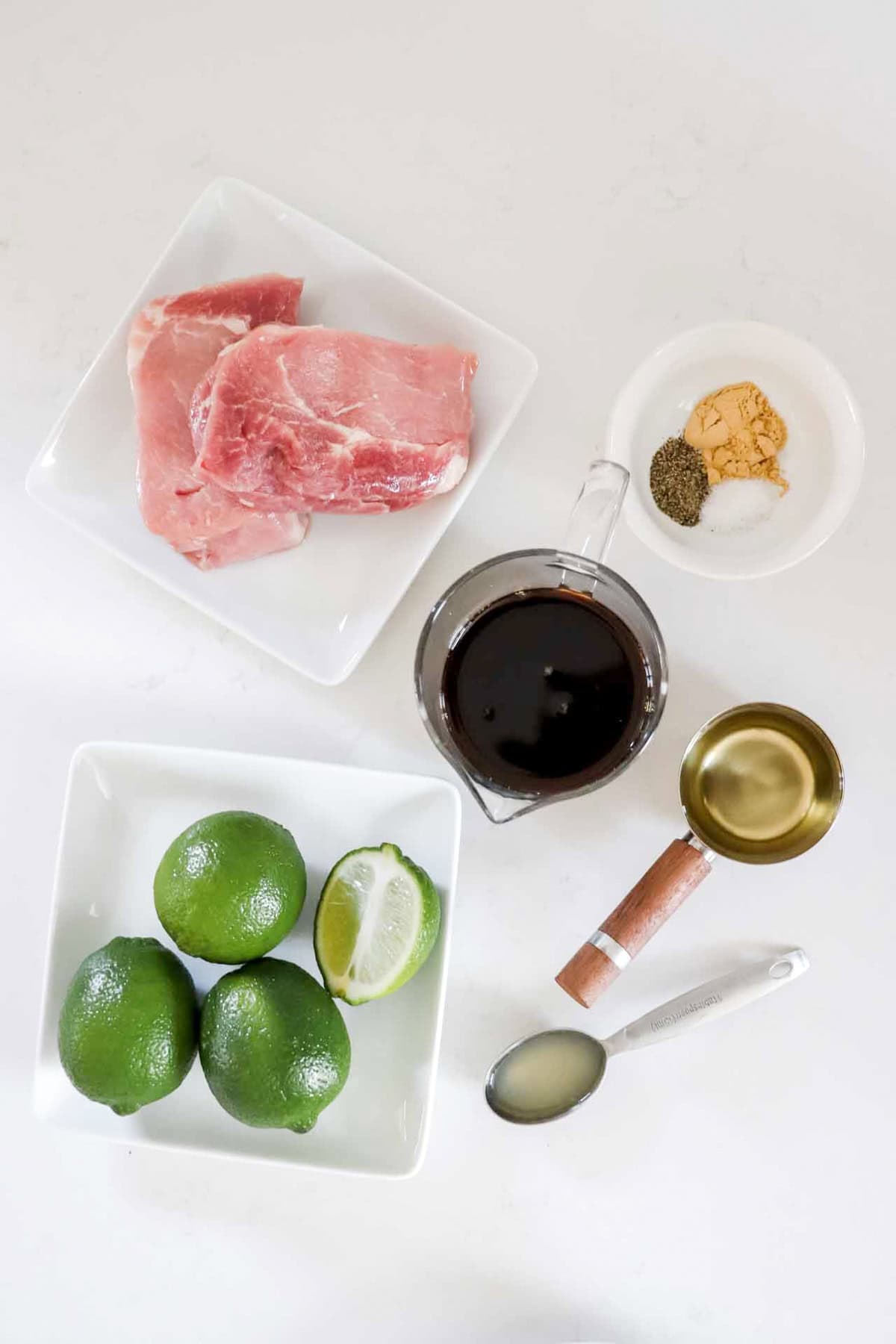 Prok Bites ingredients laid out to make pork bites. Pork chops, coconut amino, olive oil, limes and spices. www.atwistedplate.com/pork-bites