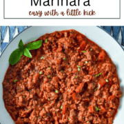 A white bowl filled with chunky, red spicy sausage marinara sauce, showing bits of ground meat, herbs, and red pepper flakes.