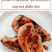 Raw chicken breasts soaking in a dark savory marinade with herbs and spices in a glass bowl.
