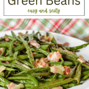 A white oval serving bowl filled with roasted green beans and crispy chopped bacon bits, served with a silver spoon.