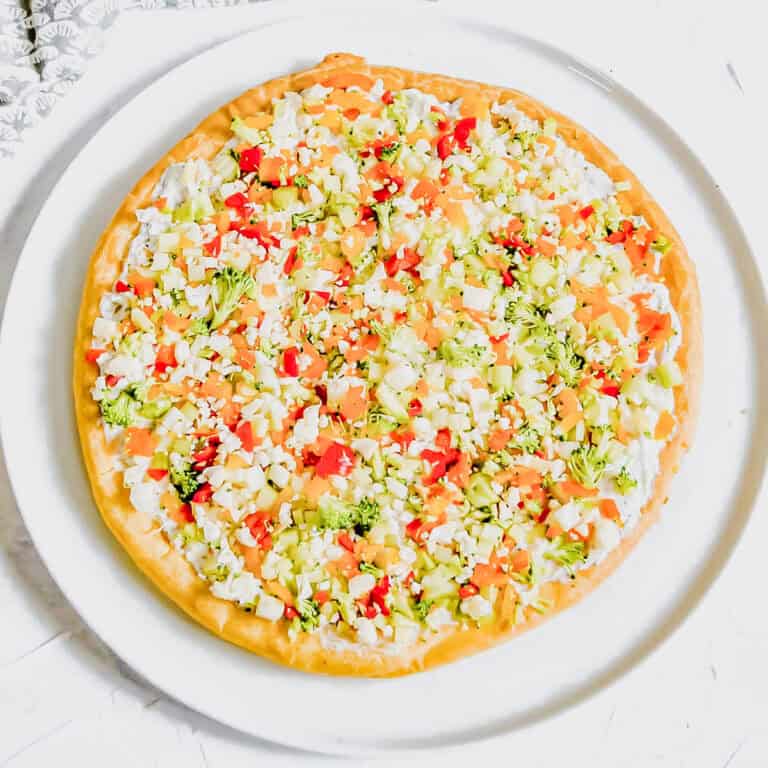Top view of vegetable pizza against a white background with red, yellow and orange peppers, and a silver pizza cutter. www.atwistedplate.com/veggie-pizza/