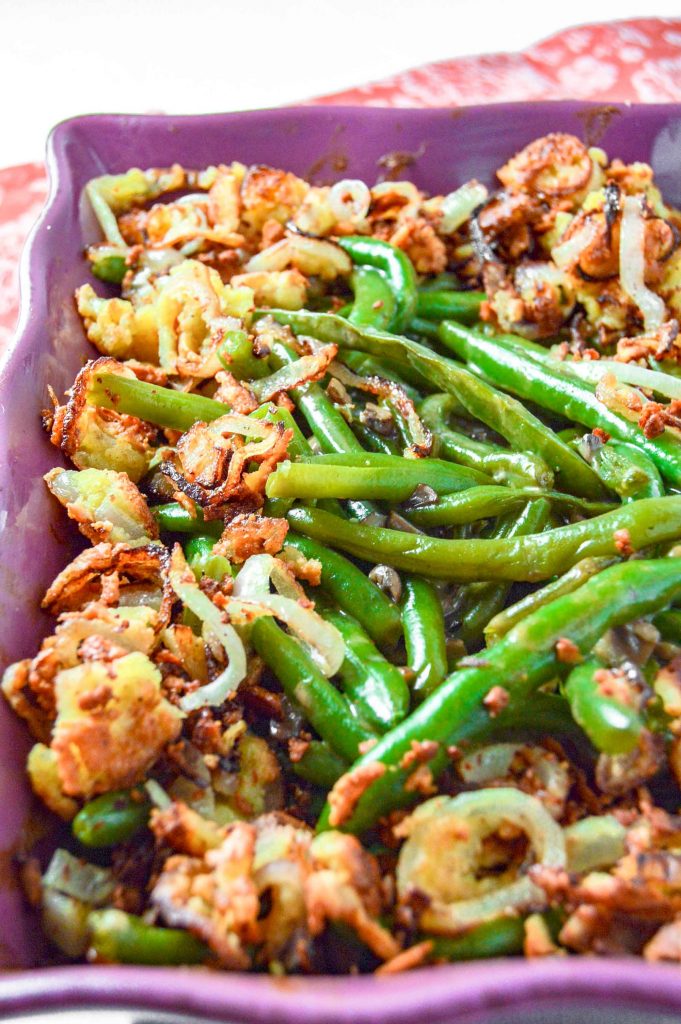 Close up angle view of Dairy Free Green Bean Casserole in a purple dish on a pink towel.  https://www.atwistedplate.com/green-bean-casserole-gluten-dairy-free/