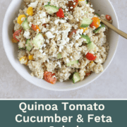 A vibrant bowl of fluffy quinoa mixed with diced red tomatoes, crisp green cucumbers, and crumbled white feta cheese, drizzled with herb-flecked Italian dressing