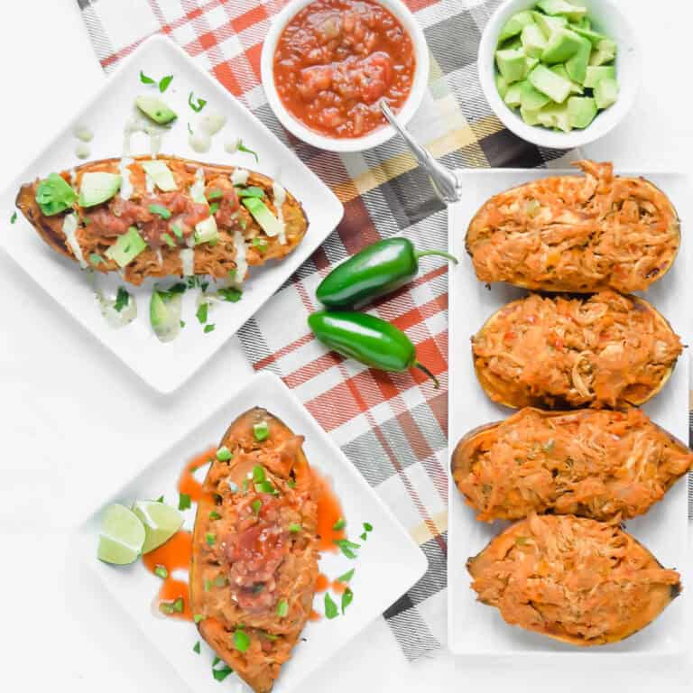 Image of two chicken stuffed sweet potatoes on white square plates. Once has avocado, salsa and ranch on it, the second has salsa, hot sauce and jalapeño. There is a rectangle plate with 4 chicken fajita stuffed sweet potatoes, bowl of salsa, bowl of avocado and 2 jalapeño on a checkered towel. www.atwistedplate.com
