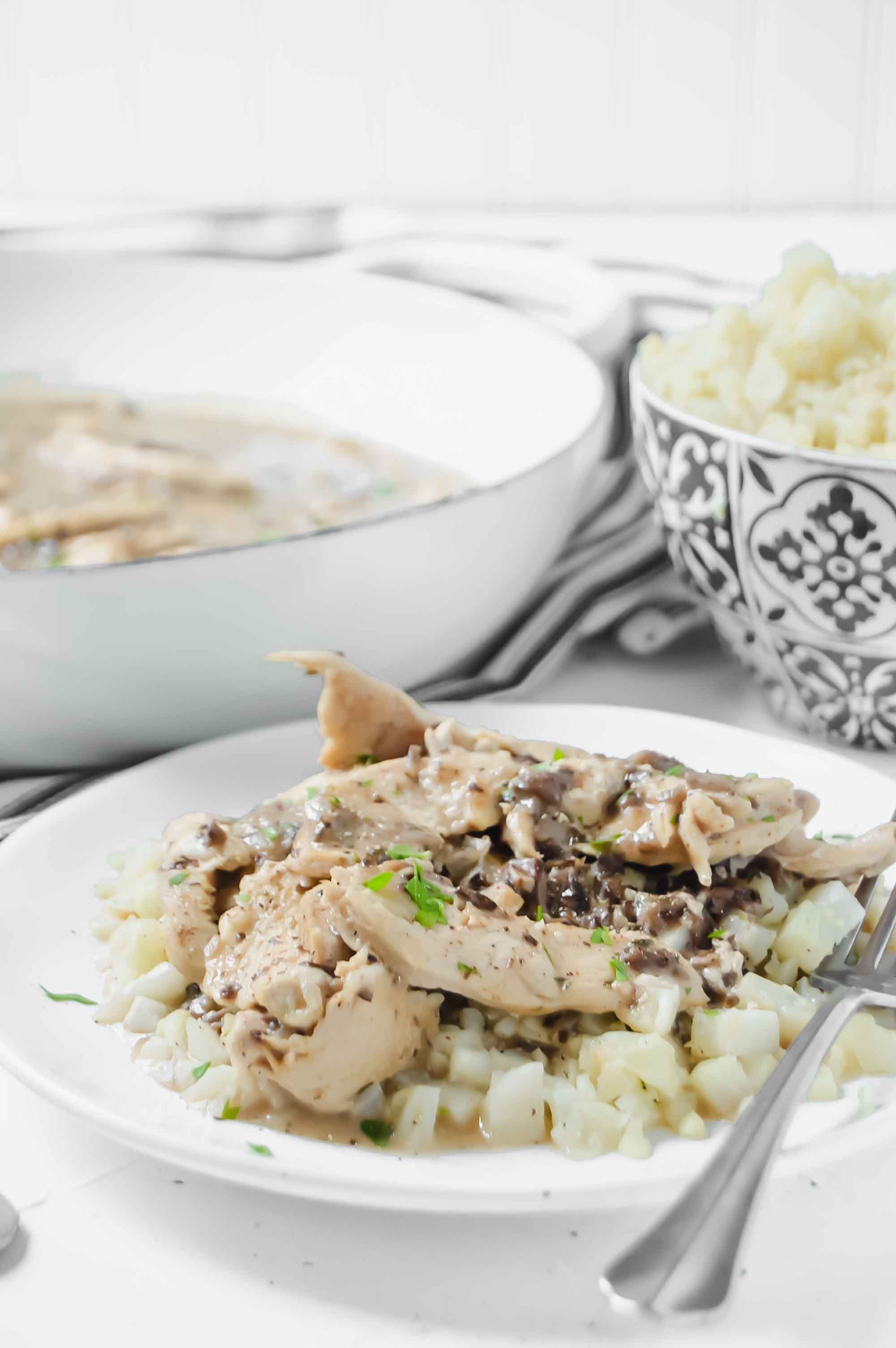 Side view plate of Creamy Chicken and Portabella Mushroom Sauce is a white dish on a black and white stripped towel. https://www.atwistedplate.com/creamy-chicken-and-mushroom-sauce/