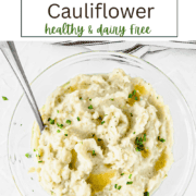 A white bowl filled with creamy mashed cauliflower topped with fresh green chives and a pat of ghee.