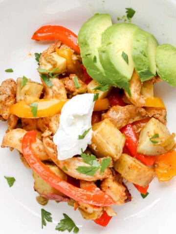 Fajita & Sweet Potato Sheet Pan Dinner in a white bowl topped with Cilantro, Sour Cream and Avocado. https://www.atwistedplate.com/fajita-sweet-potato-sheet-pan-dinner/