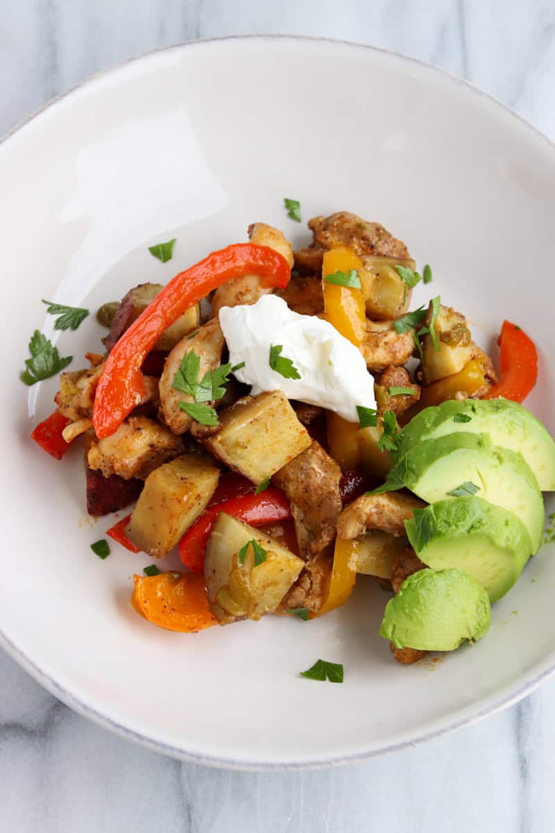 A large sheet pan filled with roasted chicken thigh strips, sliced bell peppers, red onions, and cubed sweet potatoes, all seasoned with smoky fajita spices.