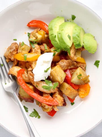 A large sheet pan filled with roasted chicken thigh strips, sliced bell peppers, red onions, and cubed sweet potatoes, all seasoned with smoky fajita spices.