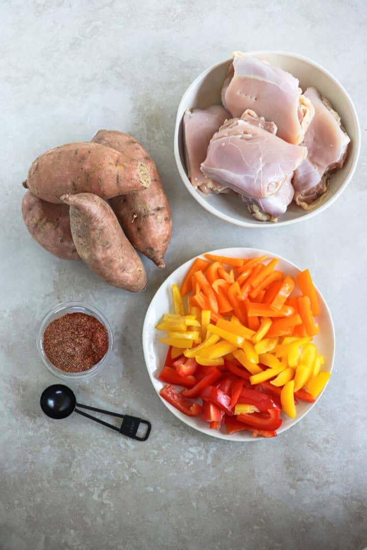 A large sheet pan filled with roasted chicken thigh strips, sliced bell peppers, red onions, and cubed sweet potatoes, all seasoned with smoky fajita spices.