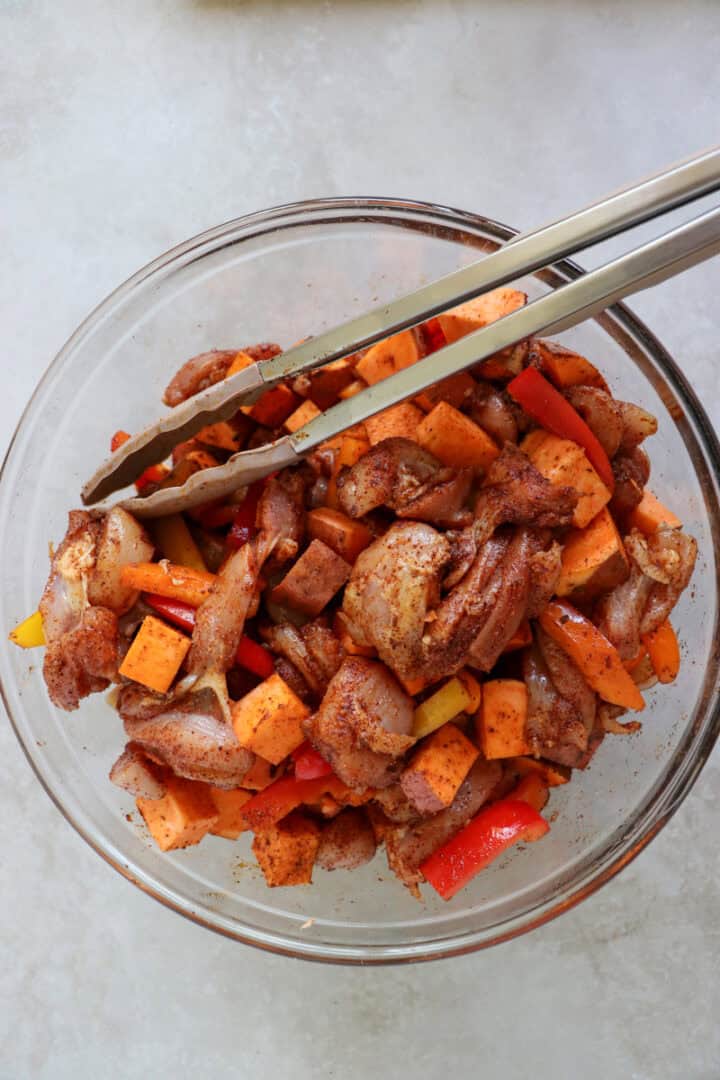A large sheet pan filled with roasted chicken thigh strips, sliced bell peppers, red onions, and cubed sweet potatoes, all seasoned with smoky fajita spices.
