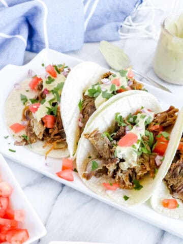 Instant Pot Pork Carnitas with Avocado Lime Aioli. Below is a white rectangle plate with 4 Carnitas topped with Onion Tomato and Avocado Lime Aioli. www.atwistedplate.com/instant-pot-pork-carnitas/