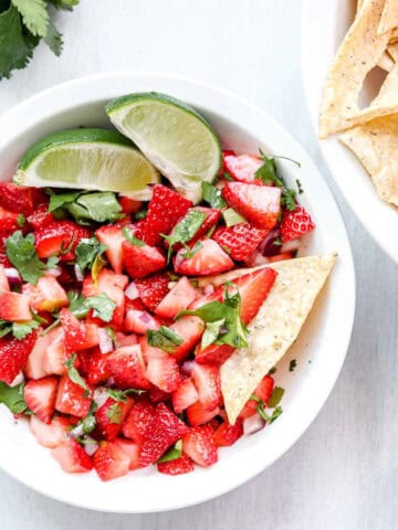 image is a bowl of Strawberry salsa with 2 lime wedges. www.atwistedplate.com/strawberry-salsa/