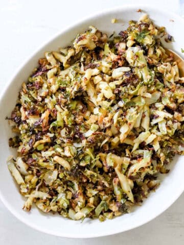 Close up of a bowl Garlic, Onion and Brussel sprouts. There is a blue towel with thin white stripes behind it. https://www.atwistedplate.com/garlic--onion-brussel-sprouts